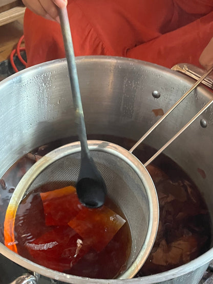 Person filtering honey from a large metal pot using a strainer.